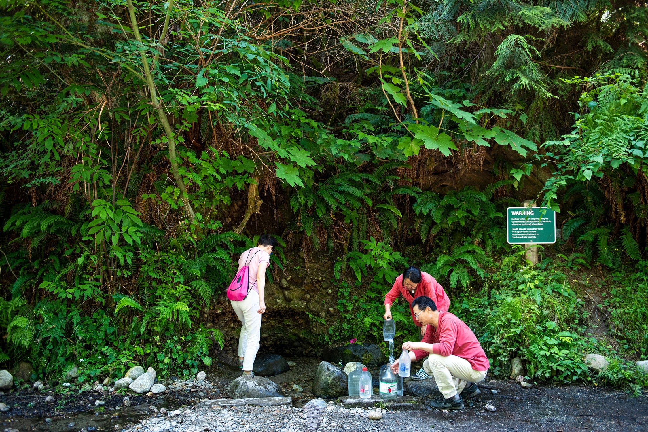 Siying Wu, Min Wu and Henry Xu collect natural spring water near the Lynn Valley Headwaters Regional Park in July 2019. (Photograph by Jimmy Jeong)