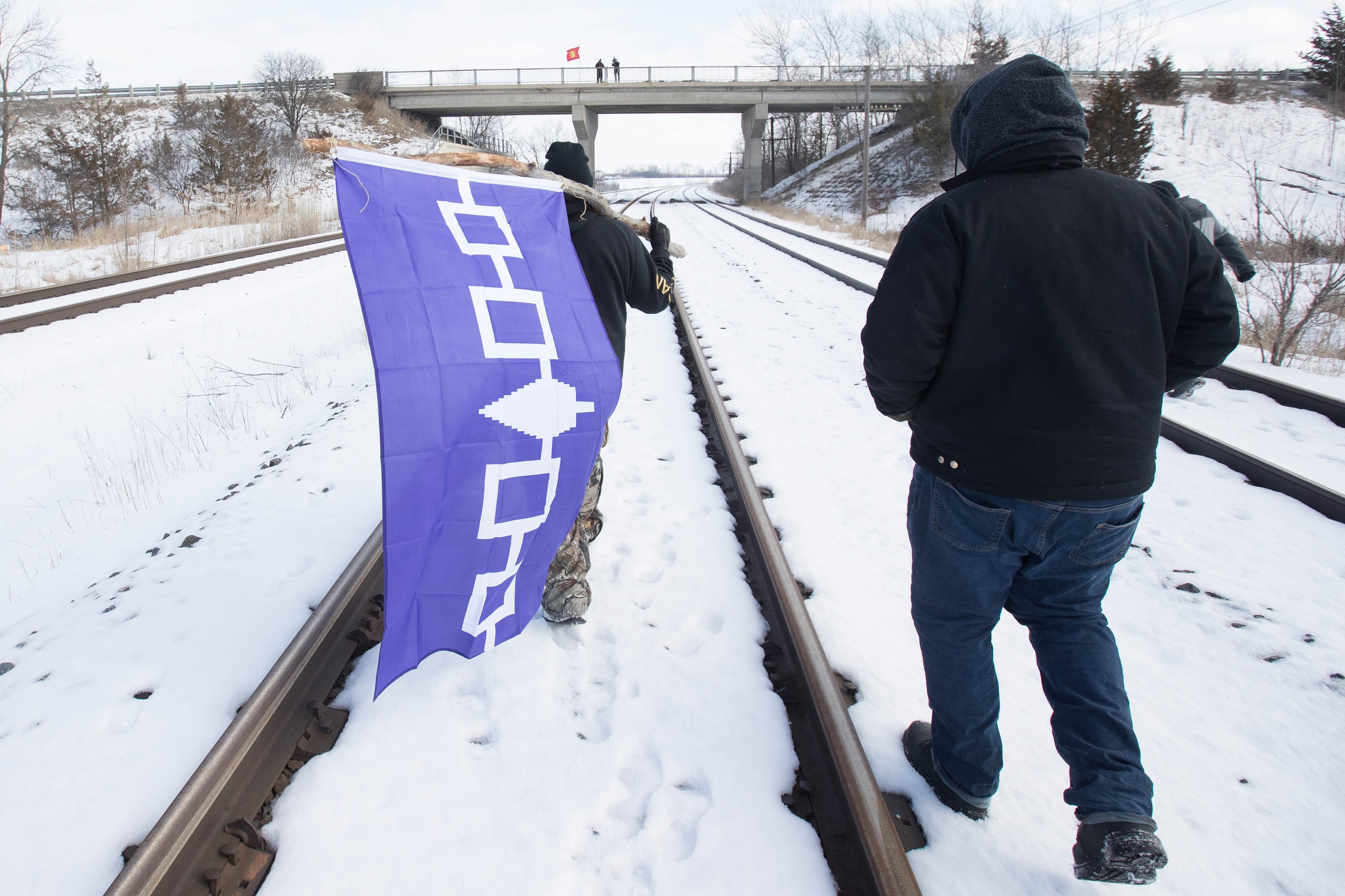 A man carries the Six Nations flag on the closed train tracks in Tyendinaga Mohawk Territory, Ont. on Wednesday, Feb. 12, 2020, in support of Wet'suwet'en's blockade of a natural gas pipeline in northern B.C. (Lars Hagberg/CP)