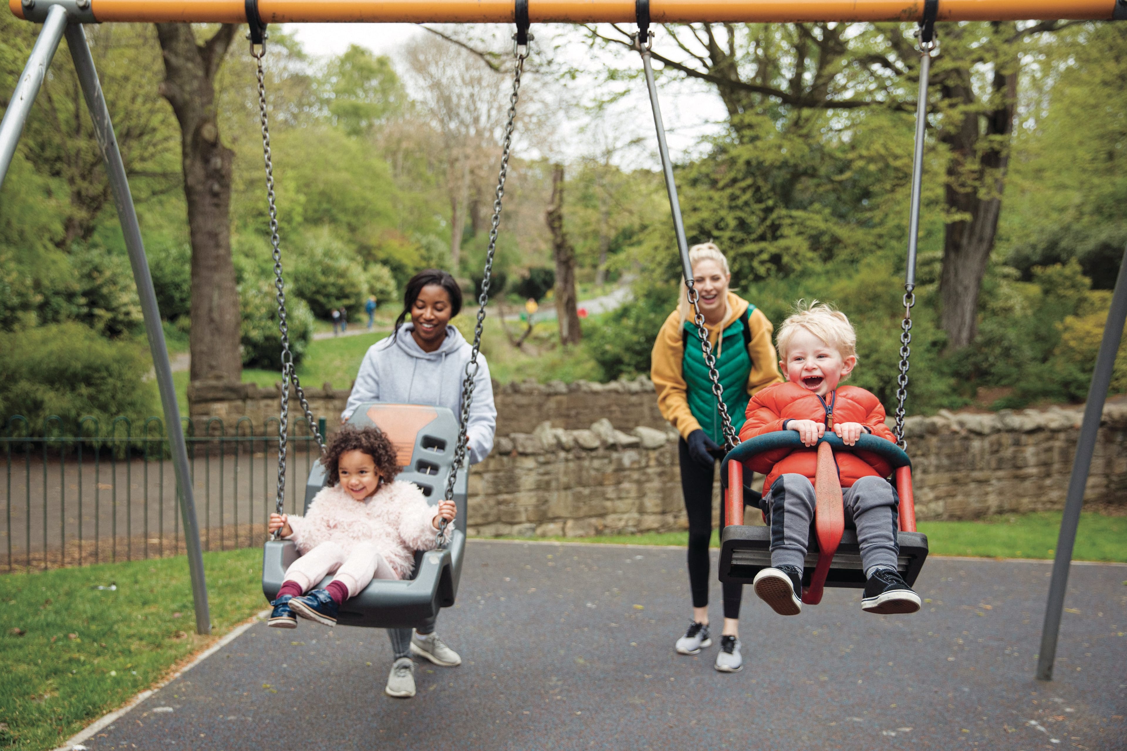 Two mothers are pushing their kids on the swings in the park. (SolStock/Getty Images)