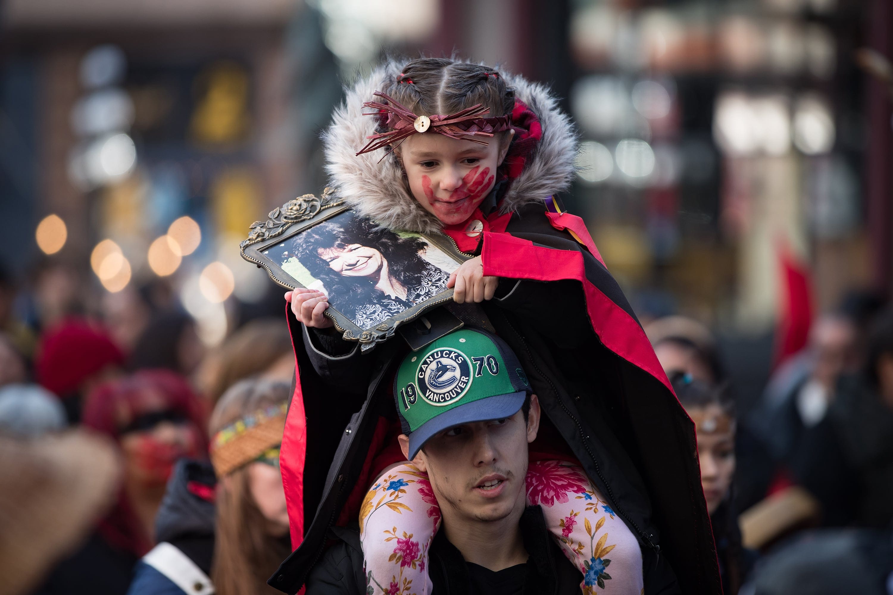 Sofia Mitchell-Schiewe holds a photo of her late grandmother Francis Mitchell while sitting on her father James Schiewe's shoulders during the annual Women's Memorial March in Vancouver, on Feb. 14, 2020 (Darryl Dyck/CP)