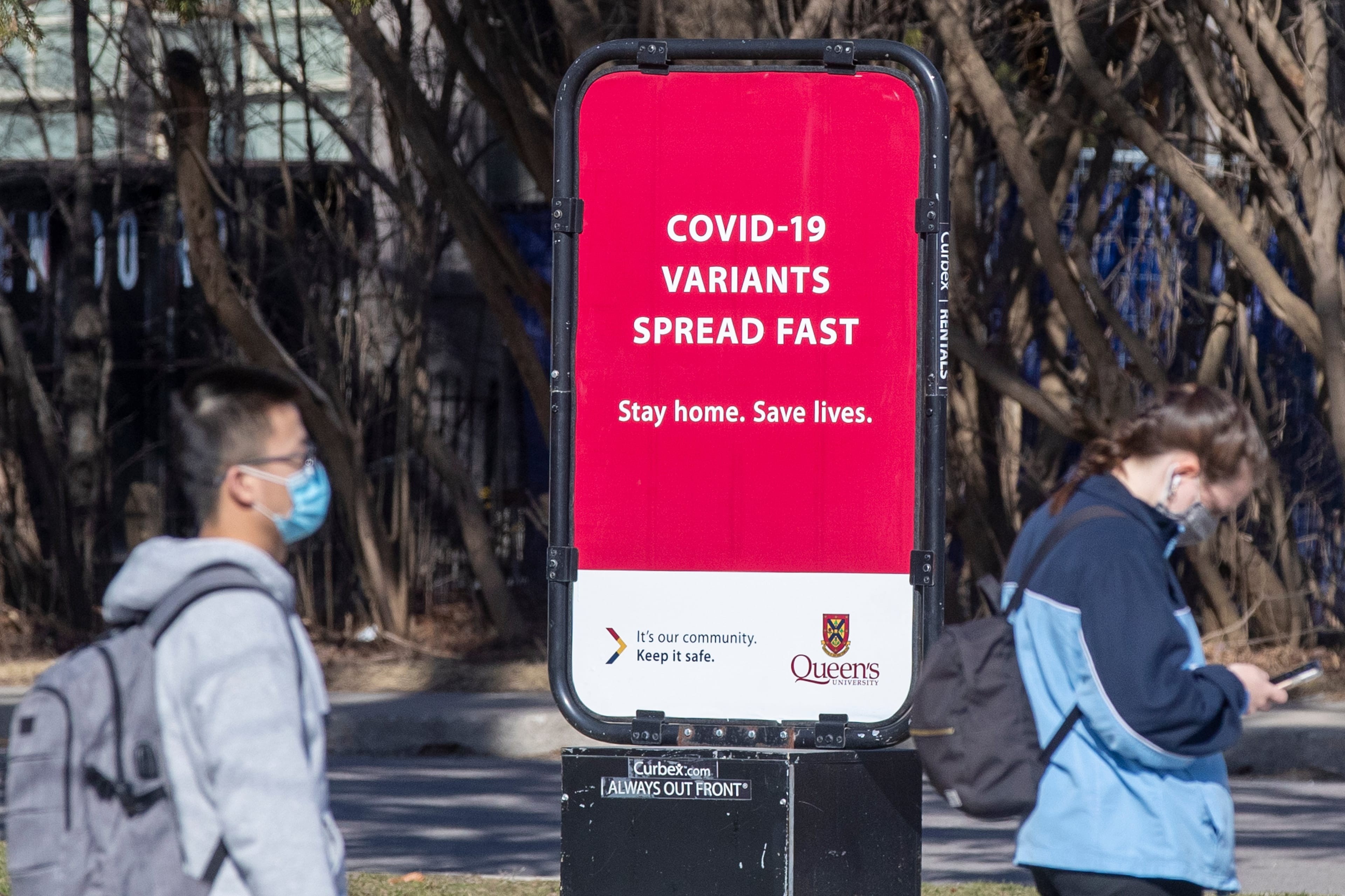 People wear masks to protect them from the COVID-19 while standing next to a information about the ongoing pandemic in Kingston, Ontario on Monday, April 5, 2021. THE CANADIAN PRESS IMAGES/Lars Hagberg