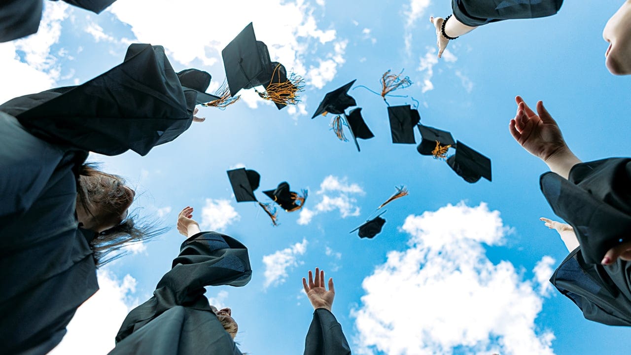 graduating students in gowns throwing caps in the air