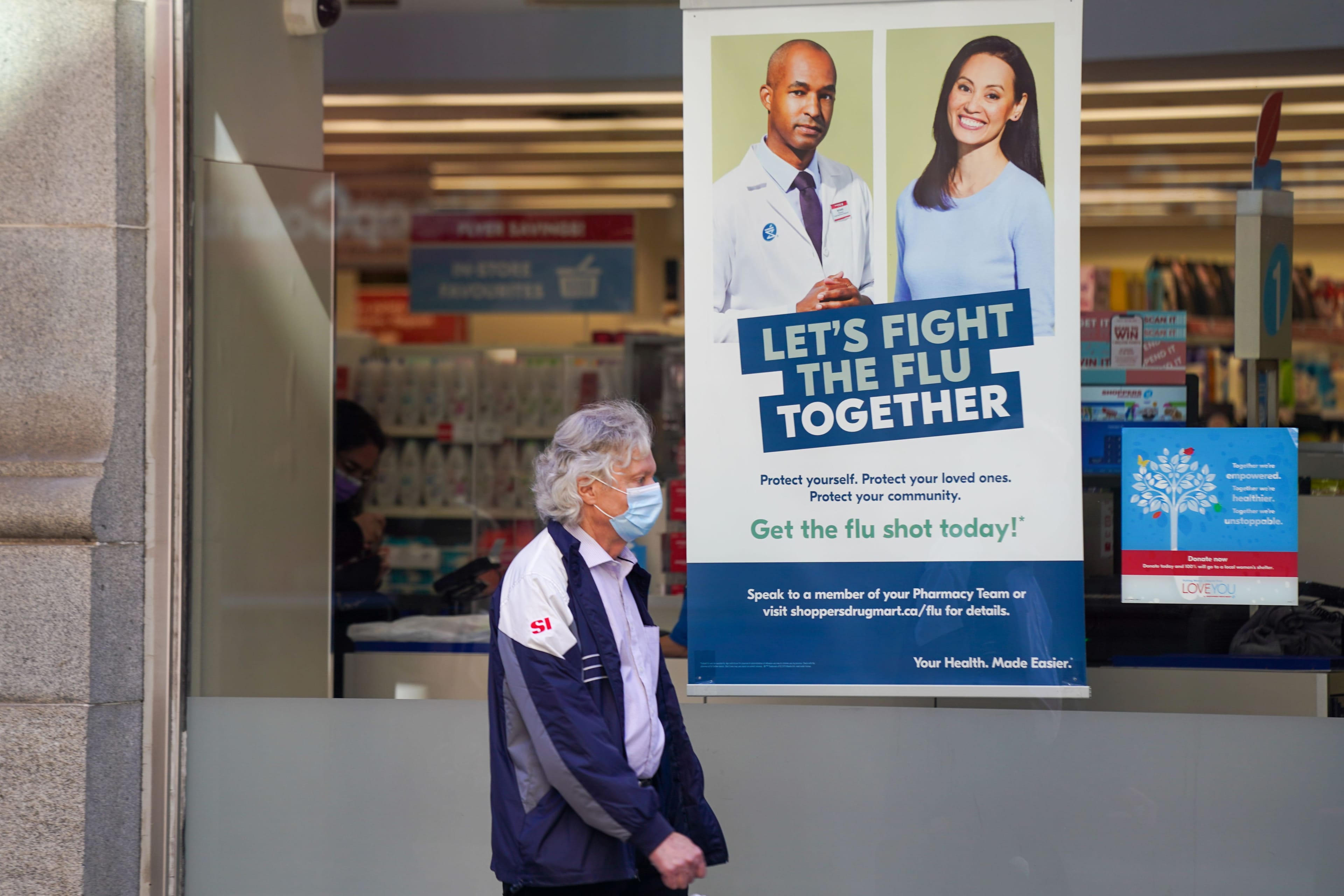 A pedestrian walks by a sign in a store window encouraging people to receive a seasonal flu shot in Toronto on Tuesday, October 19, 2021. THE CANADIAN PRESS/Evan Buhler