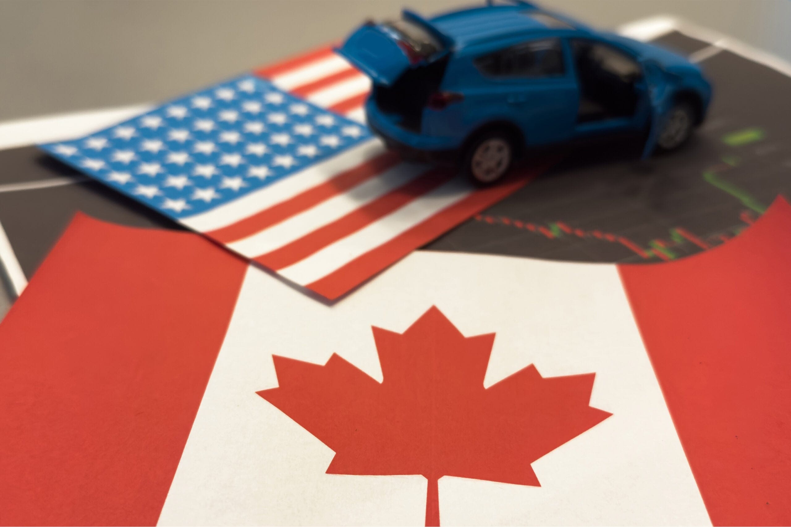 A toy car driving across an American flag and a Canadian flag