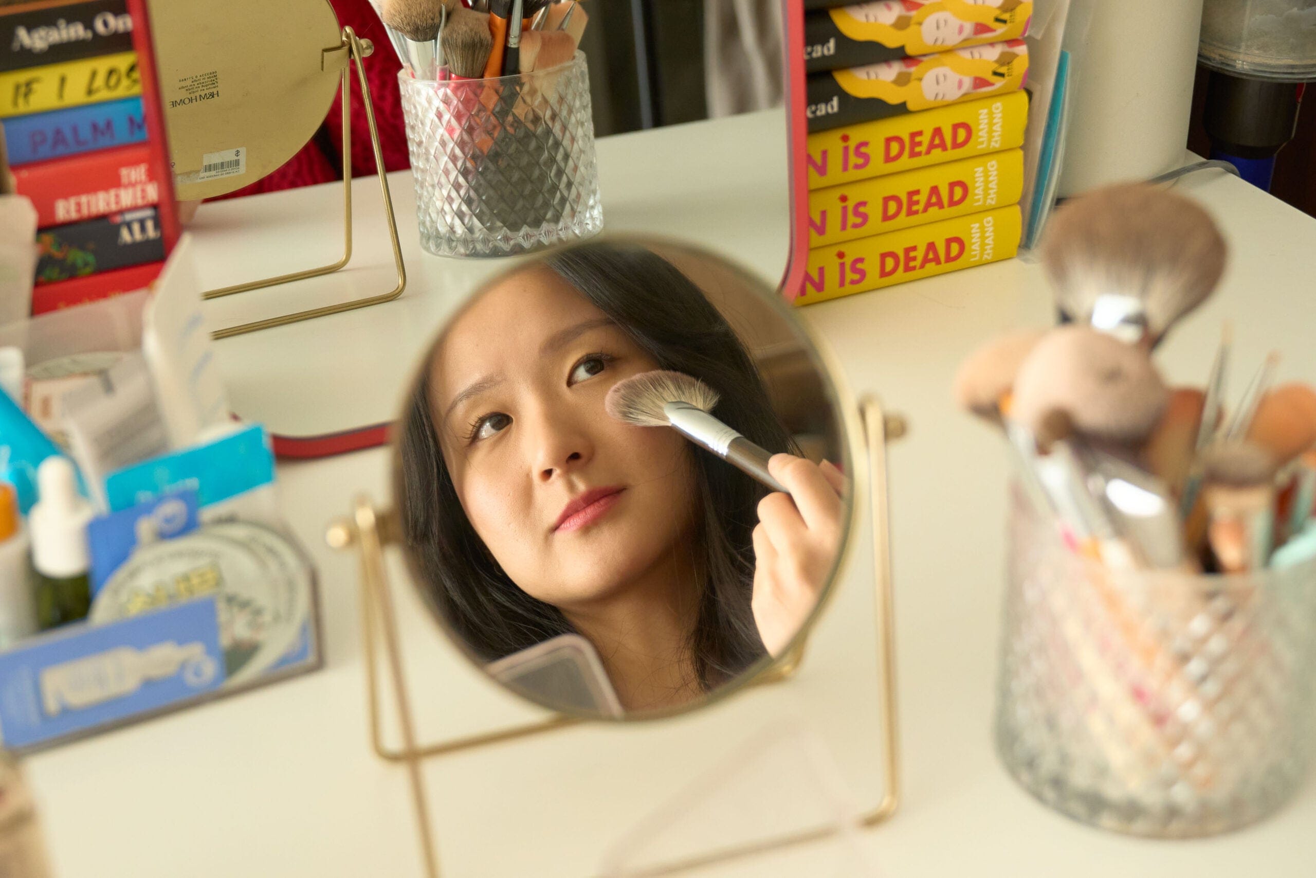 A young Chinese woman looking in a mirror and raising a makeup brush to her face