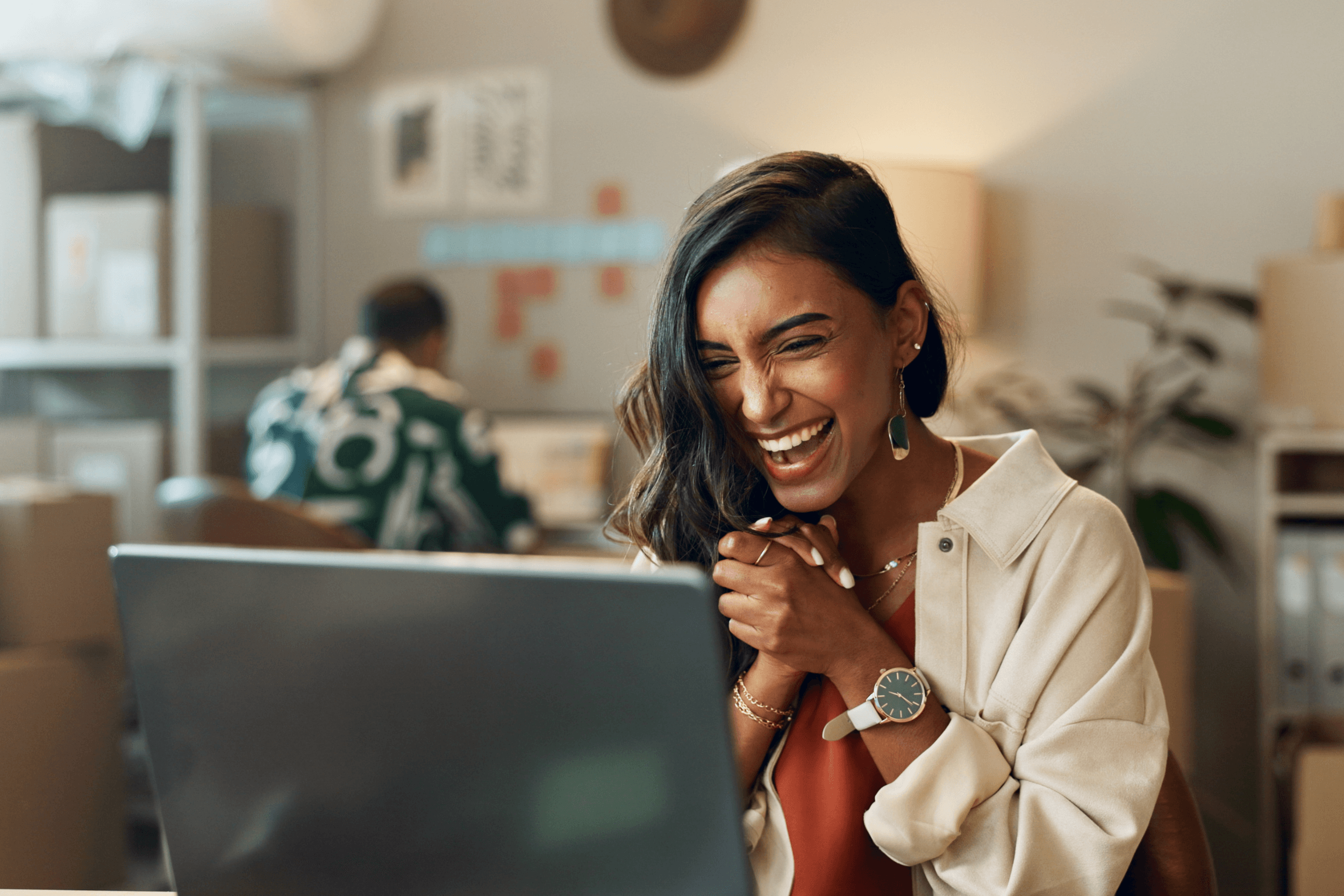A young women holds her hands together and smiles at her computer. screen