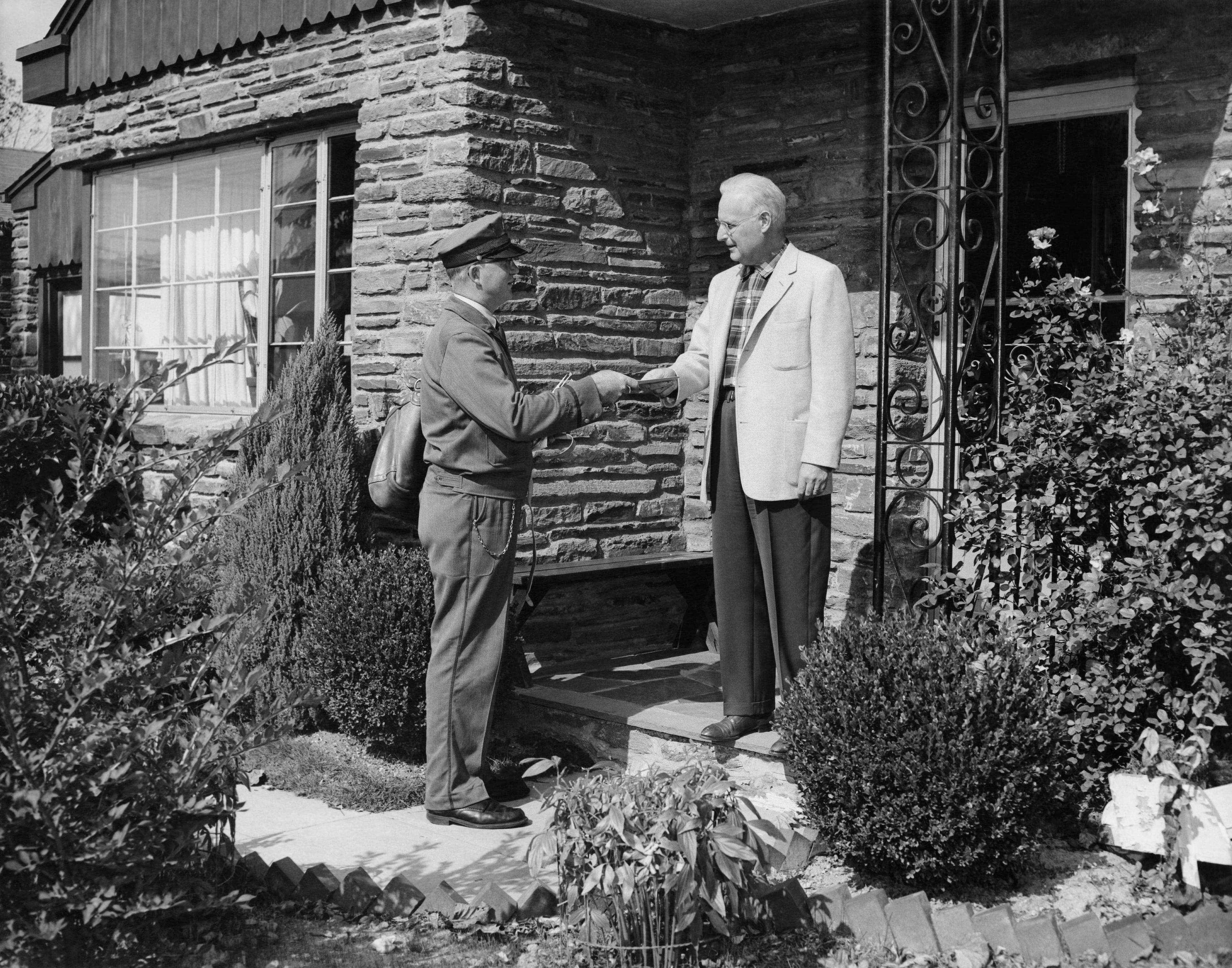 A postal worker greets an older man at this doorstep