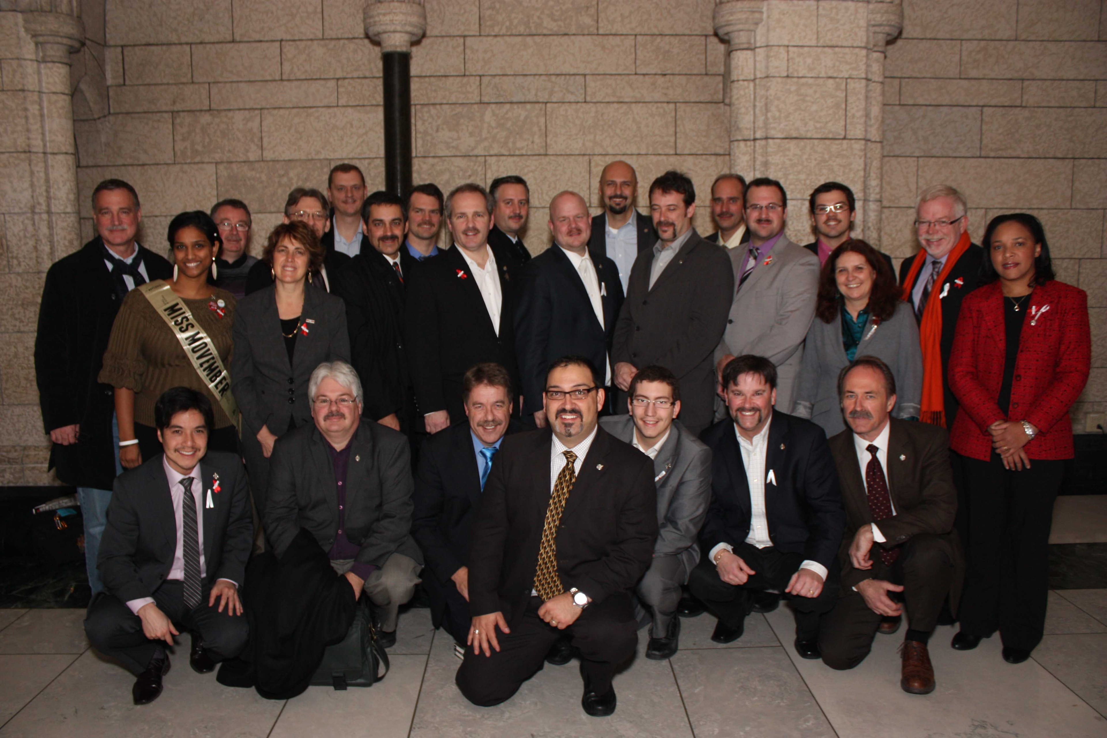 NDP male Movember participants before they shaved off their moustaches and the woman MPs who helped them raise funds.
