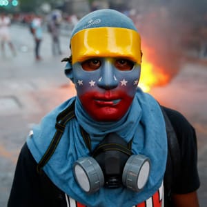 An anti-government protester, wearing a mask in the colours of the Venezuelan flag, stands at a barricade during riots in Caracas