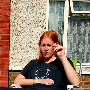A man and woman sitting outside a house smoking.