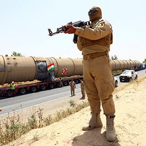 A member of the Kurdish security forces takes up position with his weapon as he guards a section of an oil refinery, which is being brought on a truck to Kalak refinery in the outskirts of Arbil