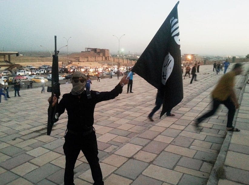 A fighter of the Islamic State of Iraq and the Levant (ISIL) holds an ISIL flag and a weapon on a street in the city of Mosul in June. (Reuters)