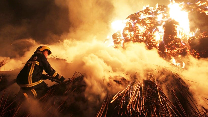 A firefighter attempts to extinguish a fire which broke out on piles of reed at a paper factory in Changde