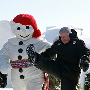 Canada's Prime Minister Stephen Harper kicks next to a Bonhomme Carnaval mascot at the Ice Hotel in Quebec City