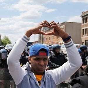 Members of the community make heart gestures with their hands in front of a line of police officers in riot gear, near a recently looted and burned CVS store in Baltimore