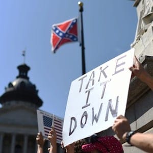 Protesters hold a sign during a rally to take down the Confederate flag at the South Carolina Statehouse, Tuesday, June 23, 2015, in Columbia, S.C. For years, South Carolina lawmakers refused to revisit the Confederate flag on Statehouse grounds, saying the law that took it off the dome was a bipartisan compromise, and renewing the debate would unnecessarily expose divisive wounds. The shooting deaths of nine people at a black church in Charleston, S.C., have reignited calls for the Confederate flag flying on the grounds of the Statehouse in Columbia to come down. (AP Photo/Rainier Ehrhardt)