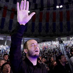 An attendee raises a hand and sings as U.S. Senator Ted Cruz, a Republican from Texas, not pictured, marks the start of his presidential campaign by giving the convocation address at Liberty University in Lynchburg, Virginia, U.S., on Monday, March 23, 2015. By kicking off his campaign at the Virginia Christian college founded by the late evangelist Jerry Falwell, rather than a venue in his home state, Cruz is signaling hell court religious conservatives as well as small-government tea-party activists as he competes to become the lead anti-establishment candidate in the party contest. Jay Paul/Bloomberg/Getty Images