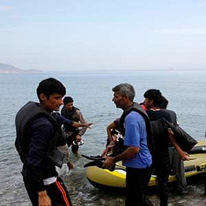 A Spanish tourist watches Pakistani migrants arriving at a beach in the Greek island of Kos after paddling an engineless dinghy from the Turkish coast August 15, 2015. United Nations refugee agency (UNHCR) called on Greece to take control of the "total chaos" on Mediterranean islands, where thousands of migrants have landed. About 124,000 have arrived this year by sea, many via Turkey, according to Vincent Cochetel, UNHCR director for Europe. REUTERS/Yannis Behrakis - RTX1OCTH