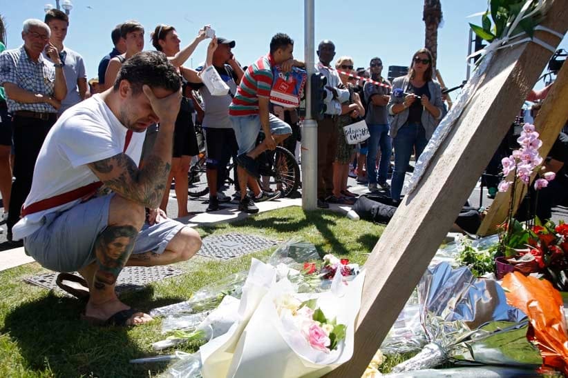 A man reacts near bouquets of flowers near the scene where a truck ran into a crowd at high speed killing scores and injuring more who were celebrating the Bastille Day national holiday, in Nice, France, July 15, 2016. (Pascal Rossignol/Reuters)