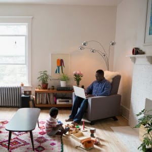 Father using laptop near son playing with toys in living room. (Hero Images/Getty Images)
