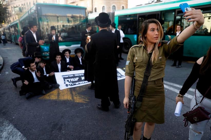 A female Israeli soldier uses her cell phone to take a selfie photograph with ultra-Orthodox Jewish demonstrators in the background who are impeding traffic by blocking a bus as they protest against Israeli army conscription in the centre of Jerusalem, on October 19, 2017. (Menahem Kahana/AFP/Getty Images)