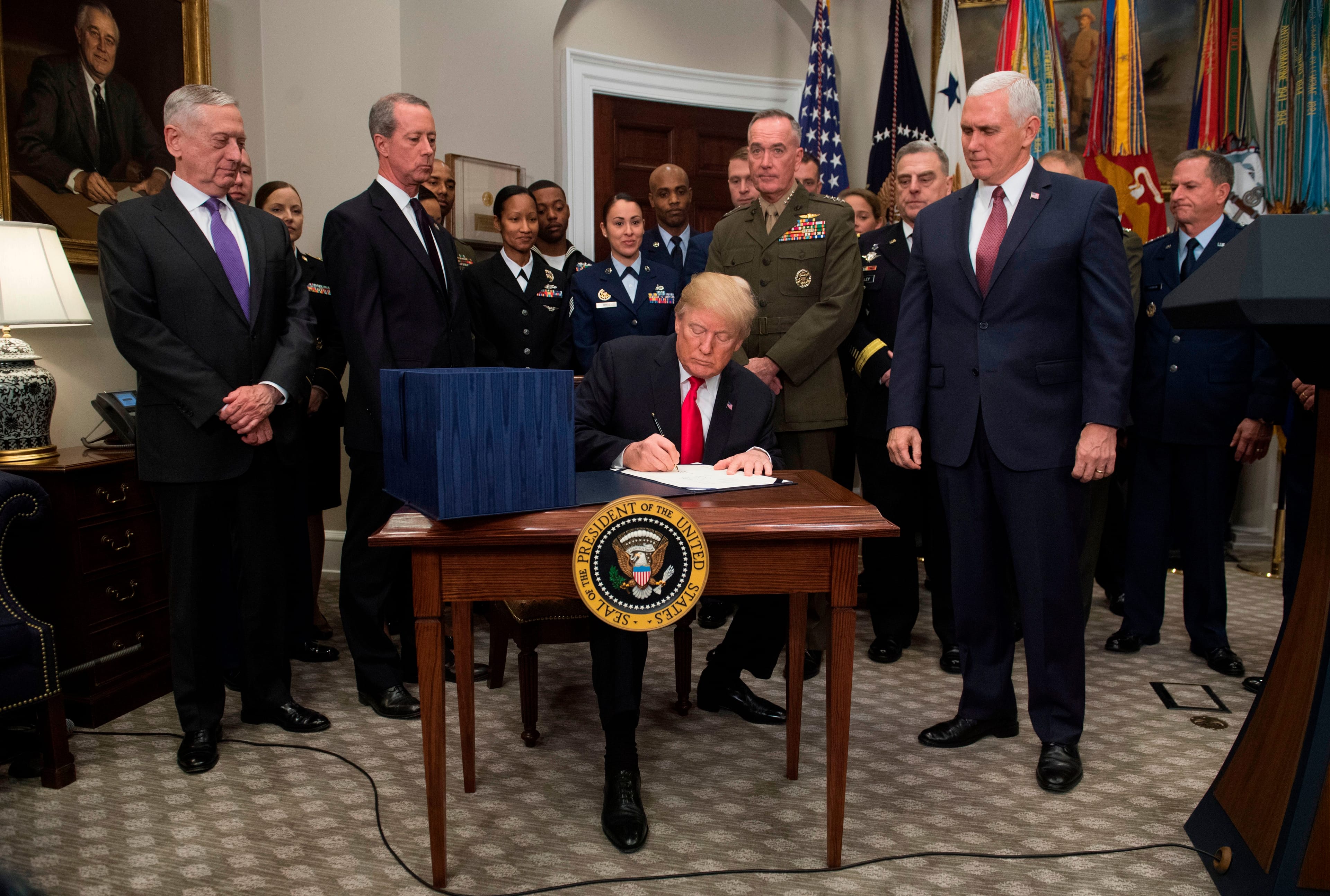U.S. President Donald Trump, surrounded by military officials and members of Congress, including Vice President Mike Pence (right) and Secretary of Defense Jim Mattis (left), signs a bill in the Roosevelt Room at the White House in Washington, DC, on Dec. 12, 2017. (Saul Loeb/AFP/Getty Images)
