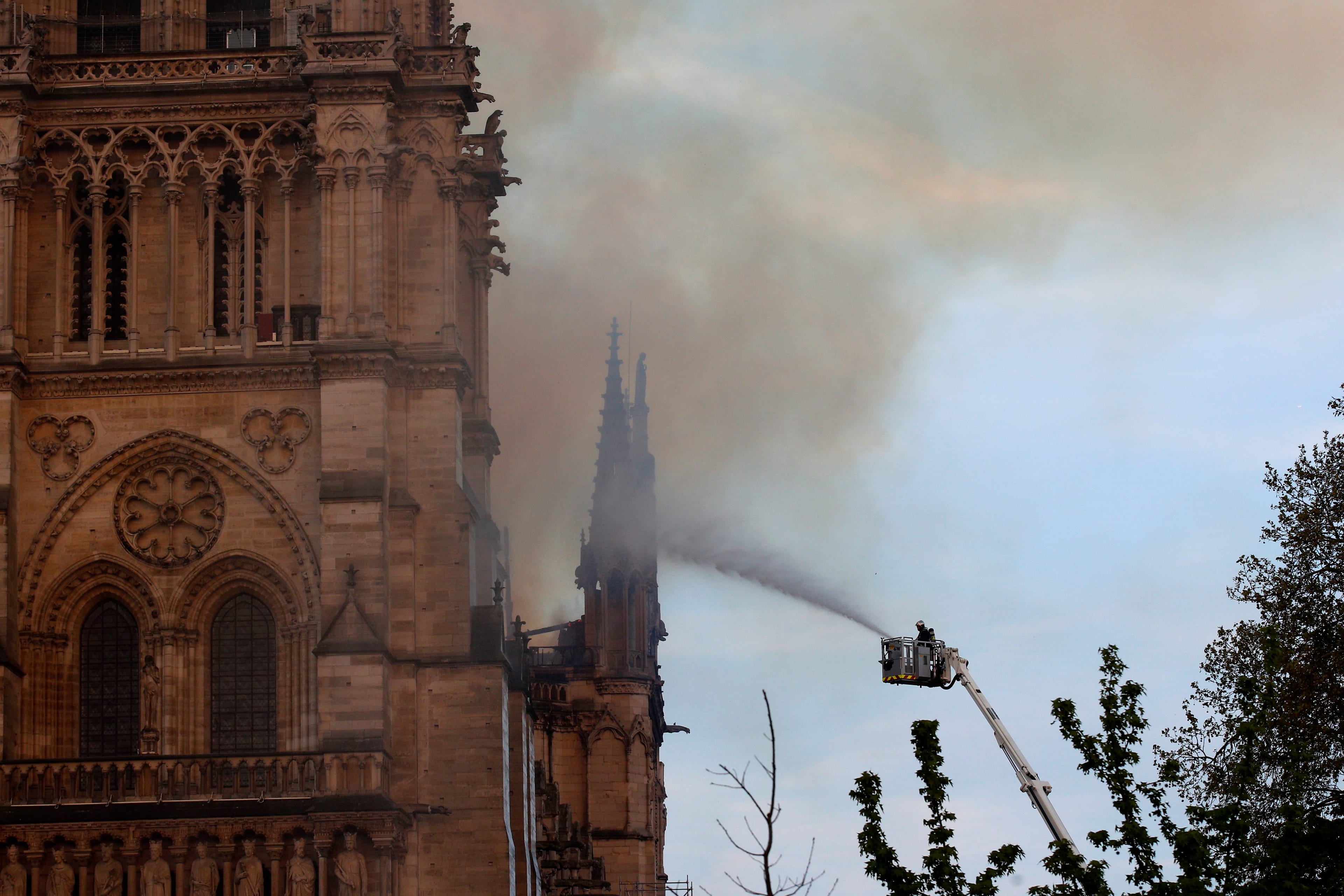 A fire fighter tackles the blaze as flames and smoke rise while Notre Dame cathedral is burning in Paris, Monday, April 15, 2019. A catastrophic fire engulfed the upper reaches of Paris' soaring Notre Dame Cathedral as it was undergoing renovations Monday, threatening one of the greatest architectural treasures of the Western world as tourists and Parisians looked on aghast from the streets below. (AP Photo/Francois Mori)