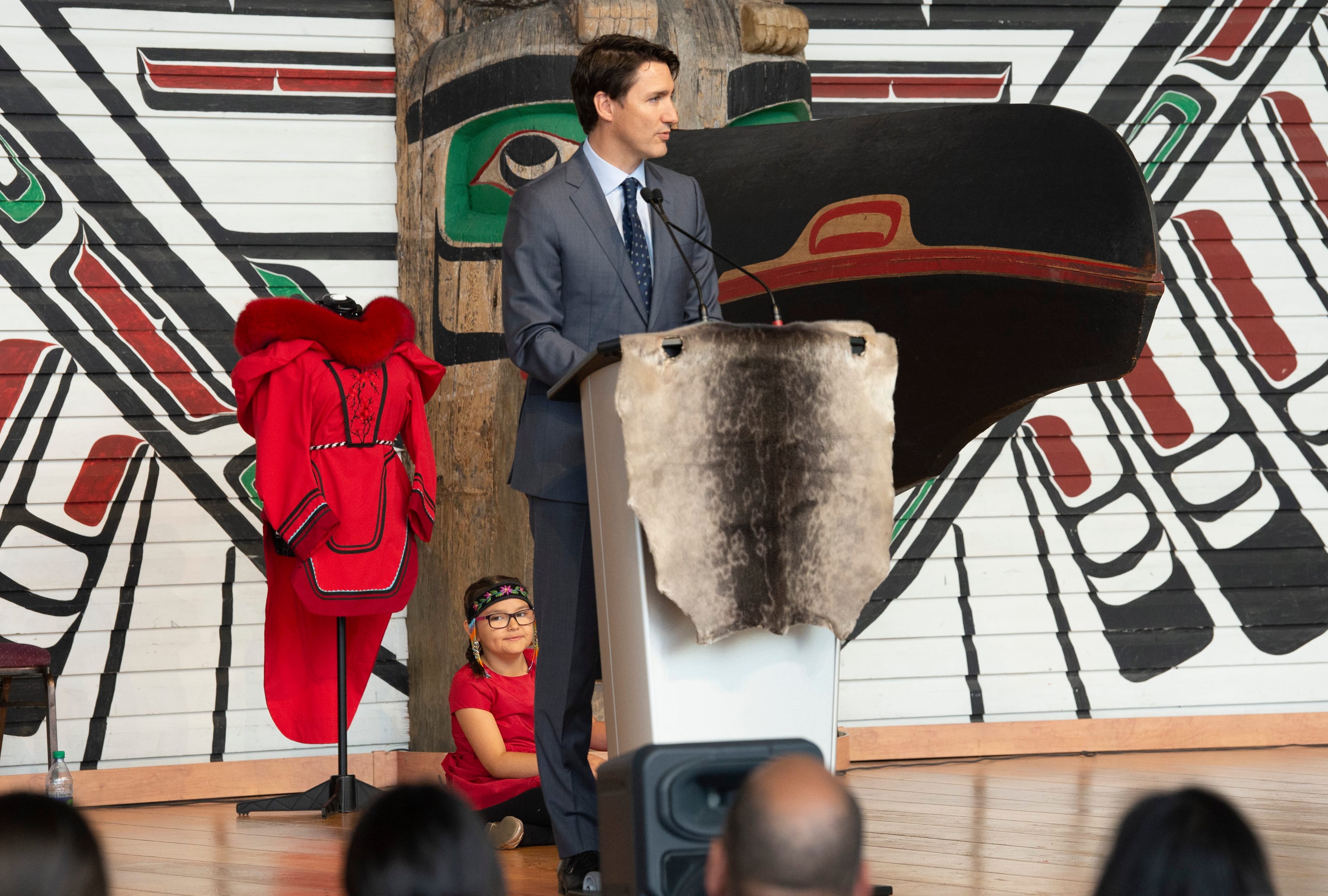 A young girl sits behind Prime Minister Justin Trudeau as he delivers his remarks during ceremonies marking the release of the Missing and Murdered Indigenous Women report in Gatineau on Jun. 3, 2019. (CP/Adrian Wyld)