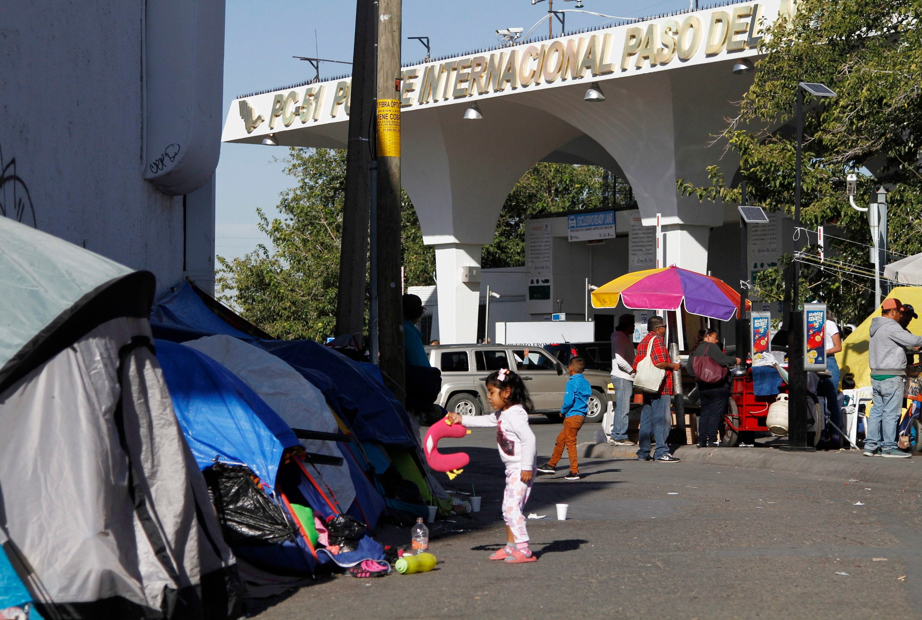 In this Thursday, Oct. 17, 2019 photo, a girl plays with a neck pillow in the street outside her family's tent in Juarez, Mexico, near the border with El Paso, Texas. (AP Photo/Cedar Attanasio, File)