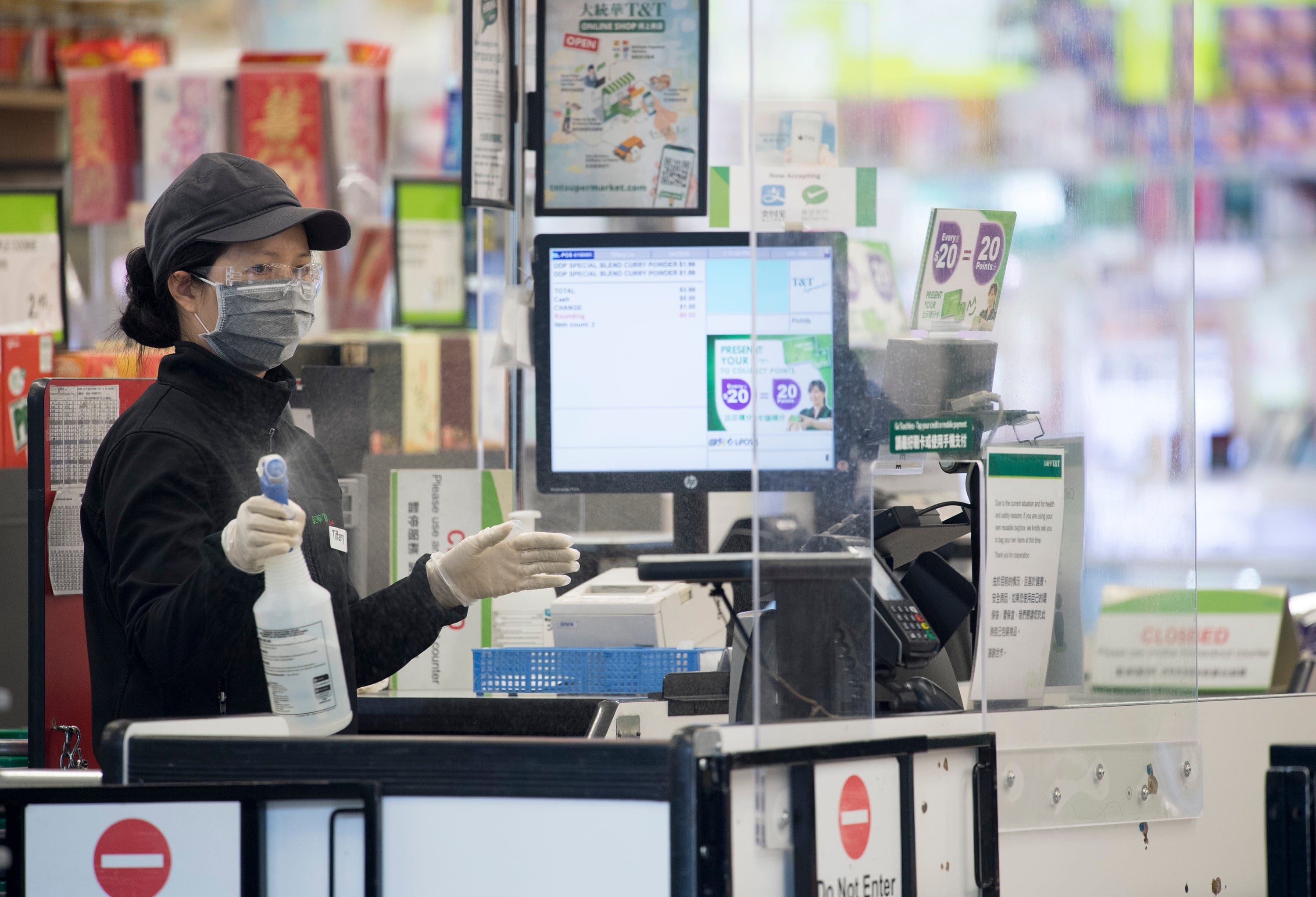 A grocery store worker clean a work space and plexiglass divider in downtown Vancouver on April 29, 2020 (Jonathan Hayward/CP)