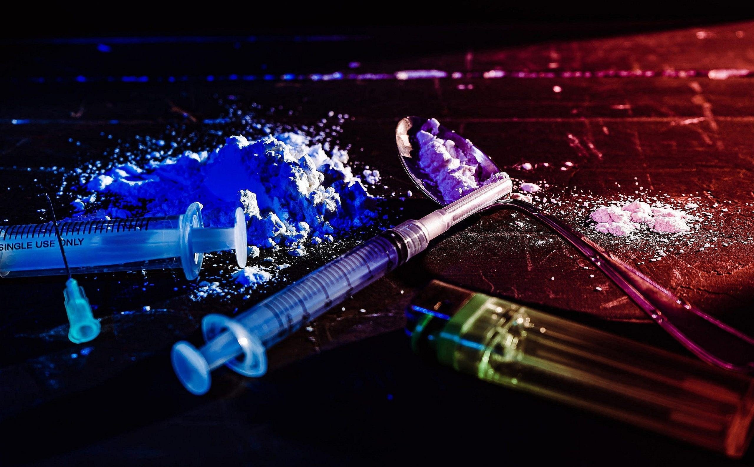 Syringes, spoon, drugs on a black, dimly lit surface. High view. Concept of illegal substances, prohibited drugs, substance abuse, hidden, illegal traffic.