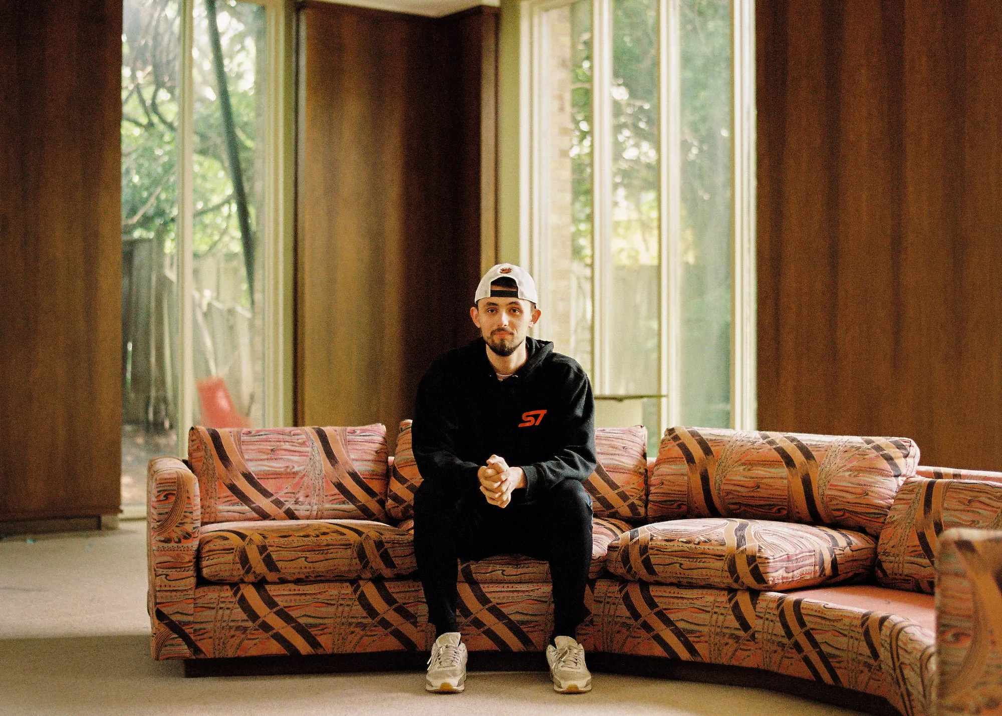 Ethan Minnie sitting on a striped pattern sofa wearing matching black hoodie and trousers.
