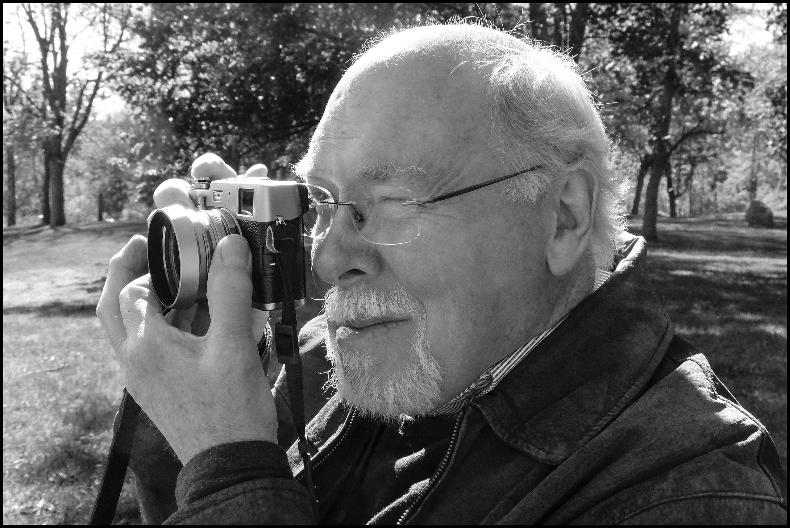 A photo of a man with a beard and glases looking through a camera viewfinder.