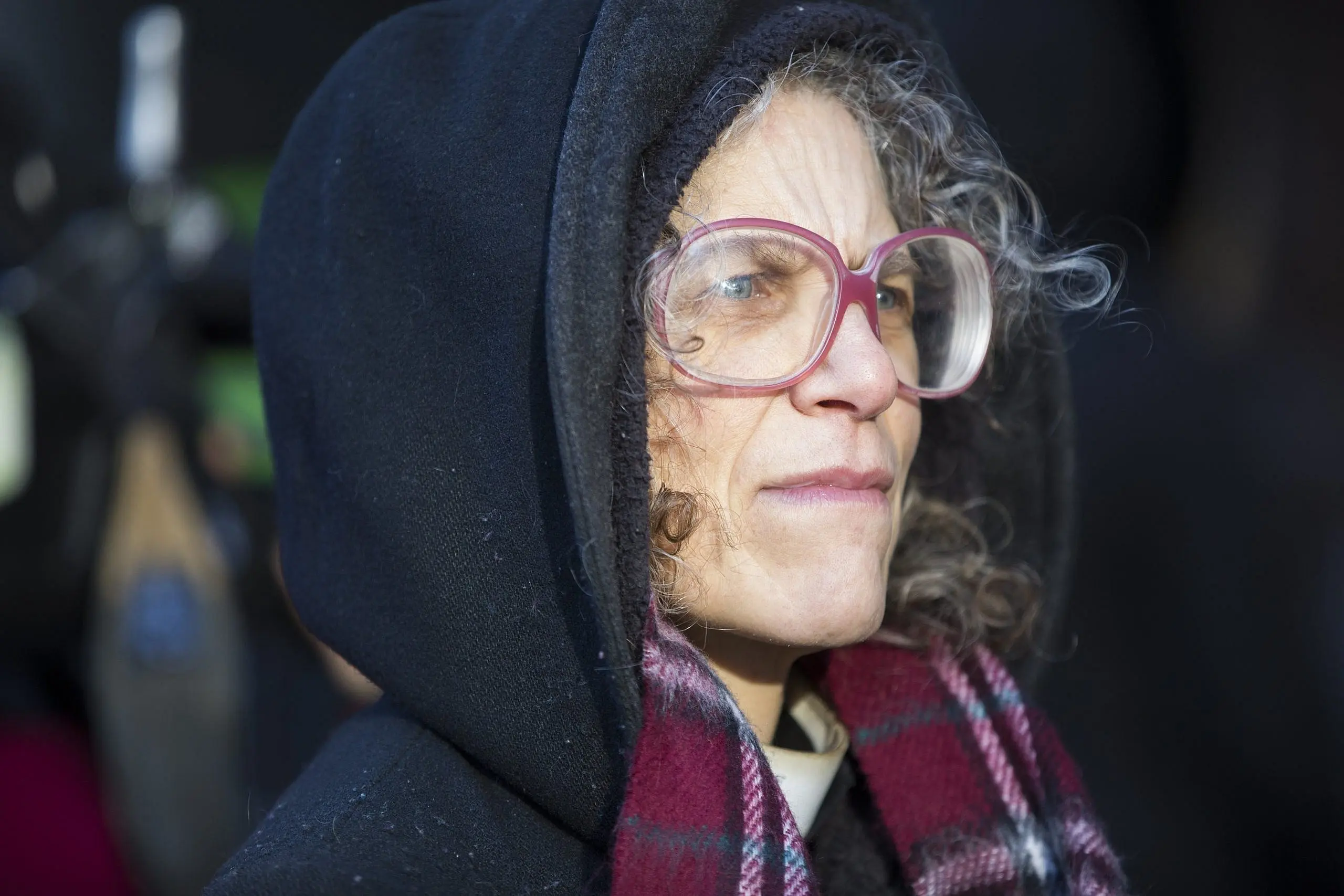 A photo of the Reverend Maggie Helwig,wearing large purple glasses and a purple scarf, looking to the side