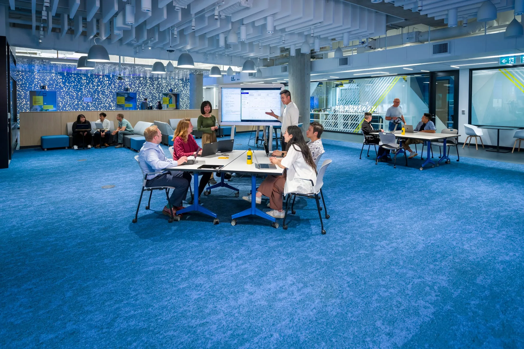 students and instructors sitting around a table talking in a large blue room