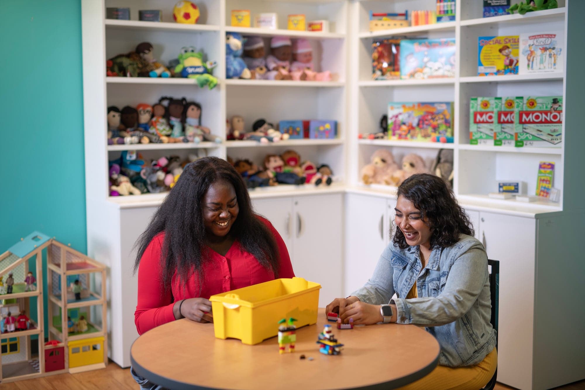 two social worker students sitting at a table surrounded by bookcases with toys and other children items
