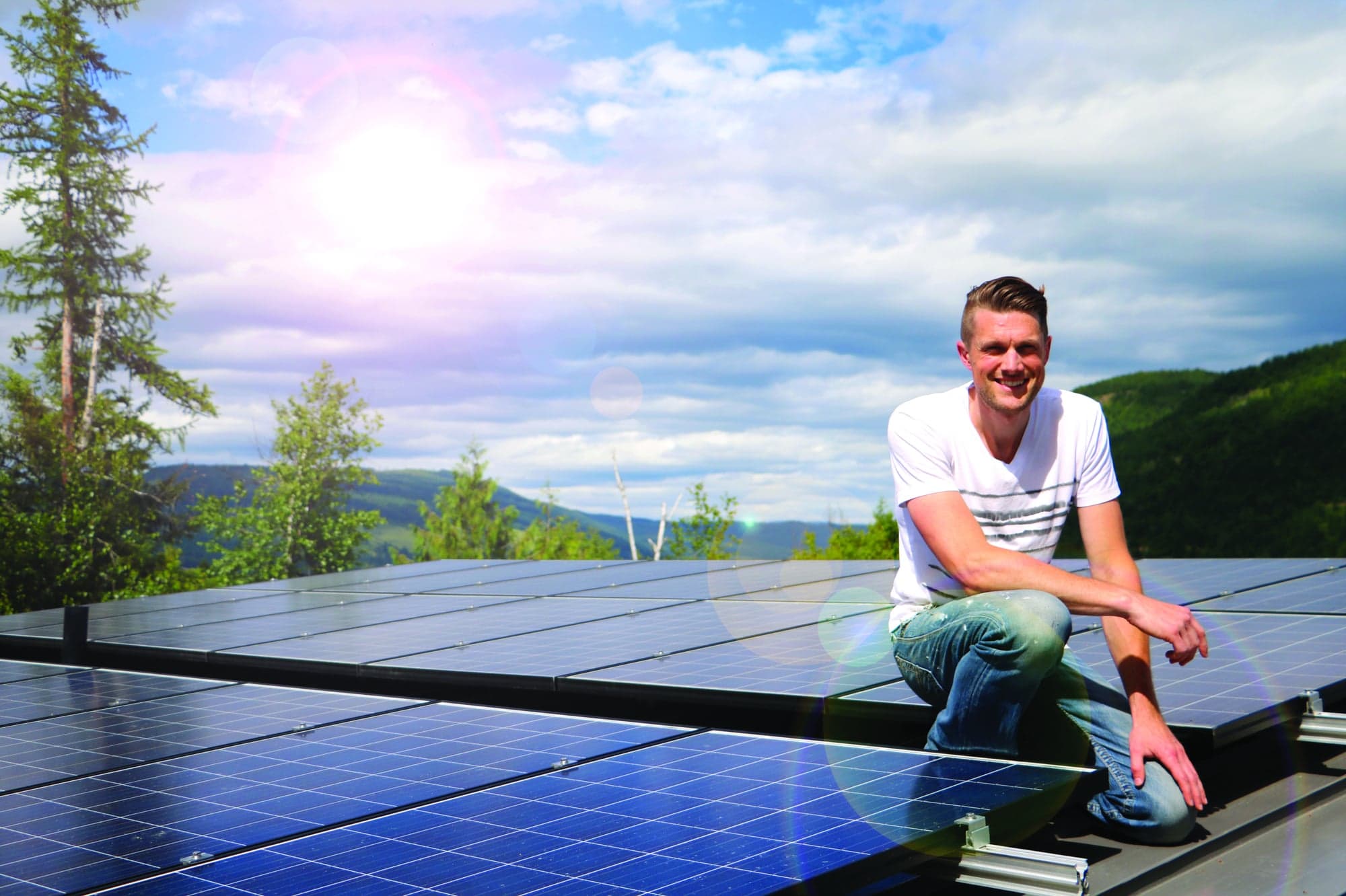 Student sitting on solar panels on top of a building with forest in the background