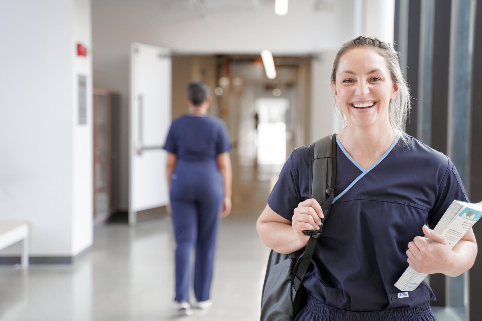 smiling student wearing scrubs standing in a hallway