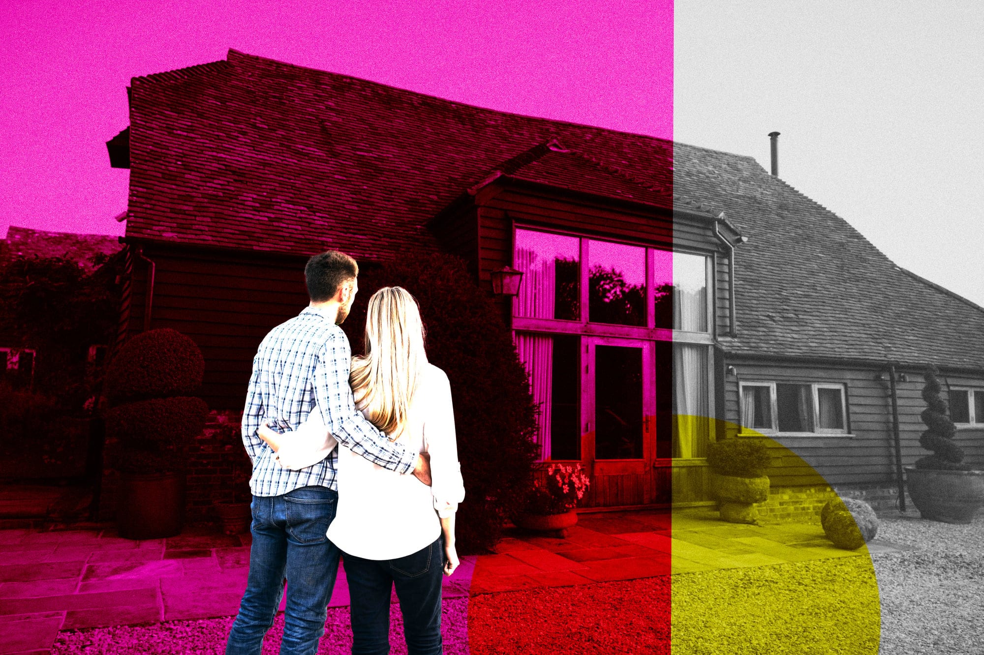 Rear view of British couple wearing casual clothing and standing with arms around each other admiring their home converted from traditional wooden barn.