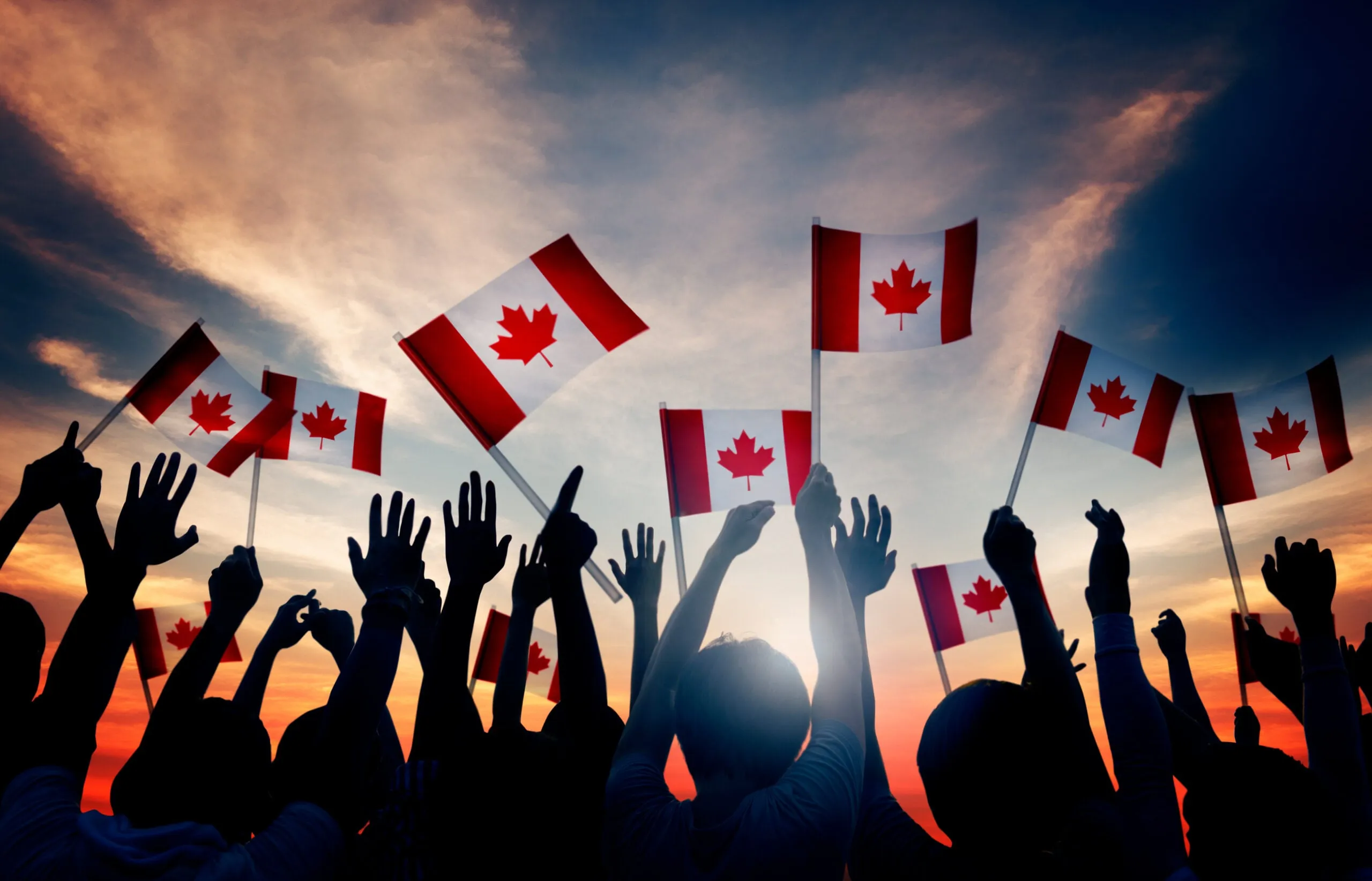 A silhouetted crowd waving Canada flags