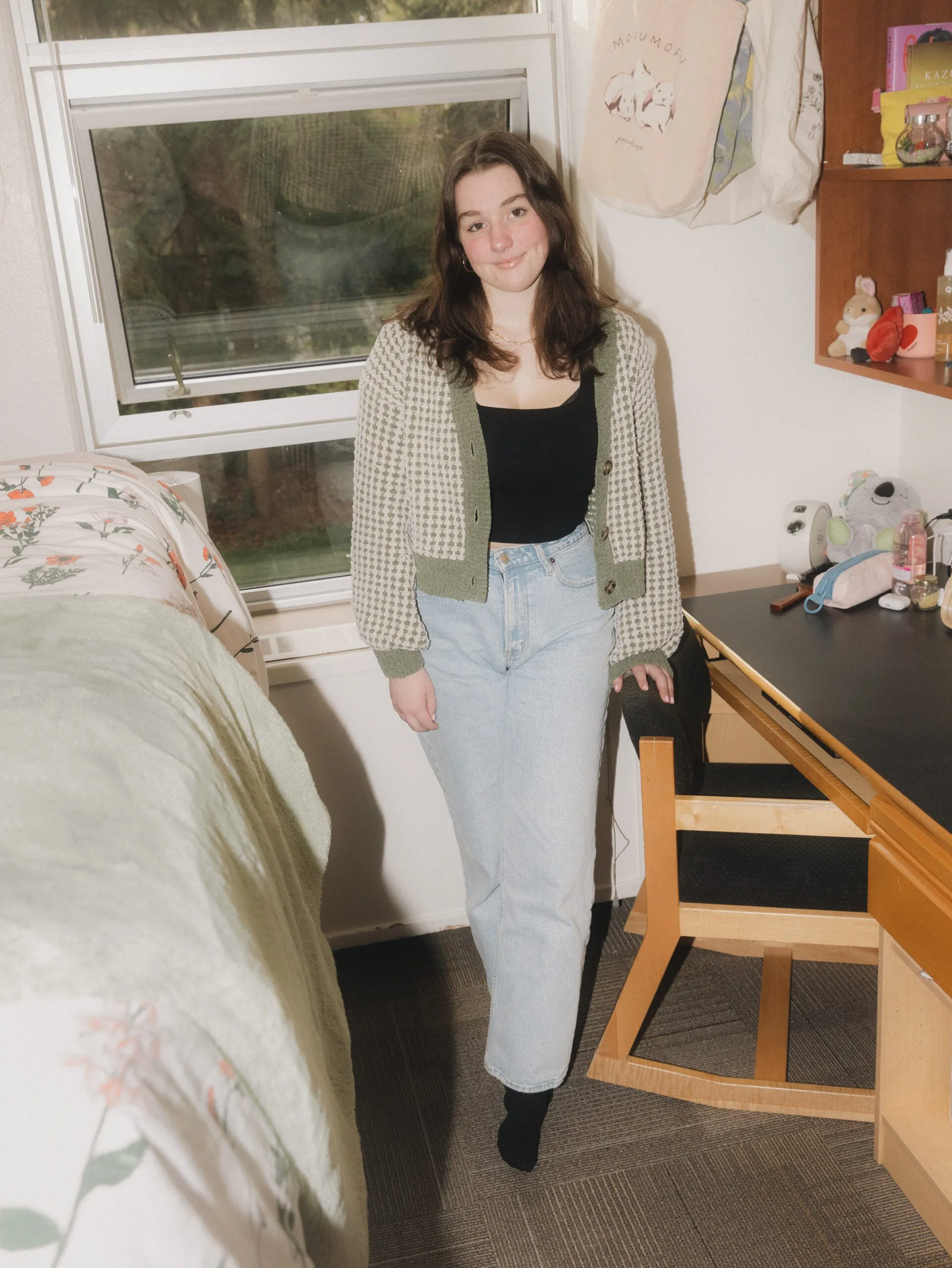 Delaney How stands between her bed and desk in a university of British Columbia dorm room