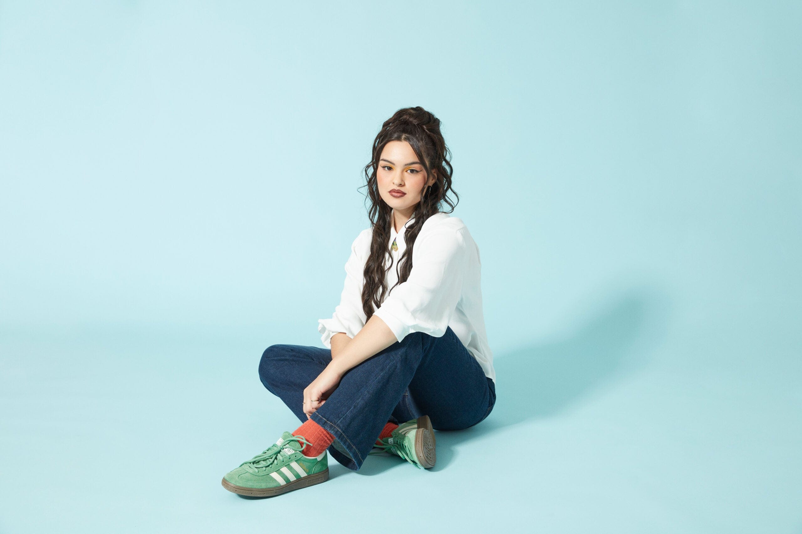Anna Lambe in a white shirt and blue jeans, photographed against a light blue background
