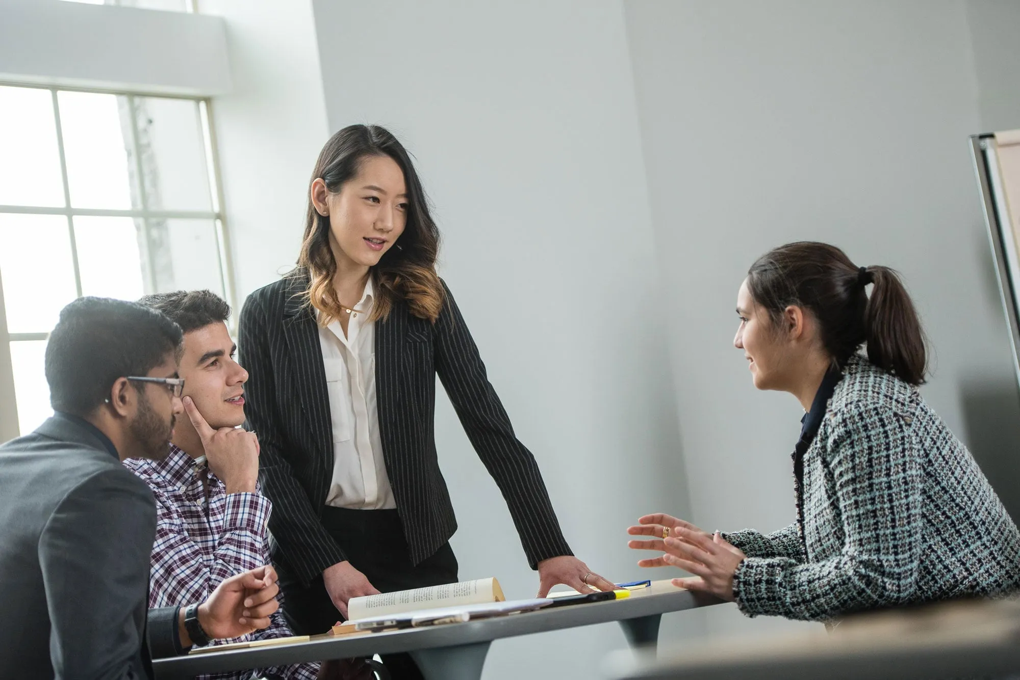 Four people talking, leaning over a table