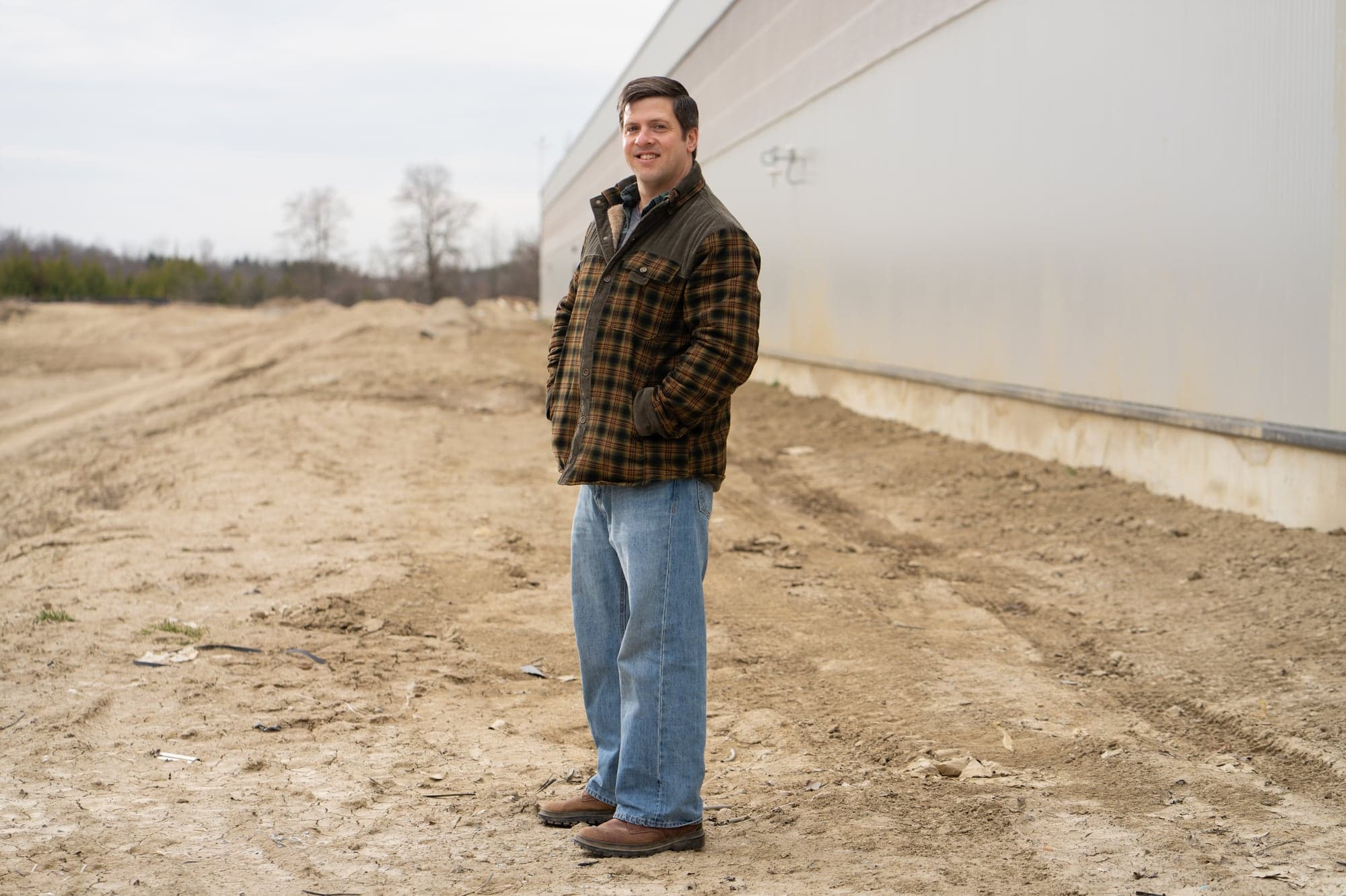 A man in a puffer coat and jeans standing on farmland