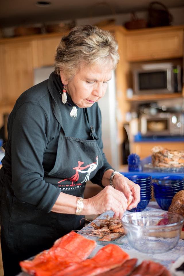A Haida Gwaii chef in a black top and black apron, standing at the counter in her kitchen