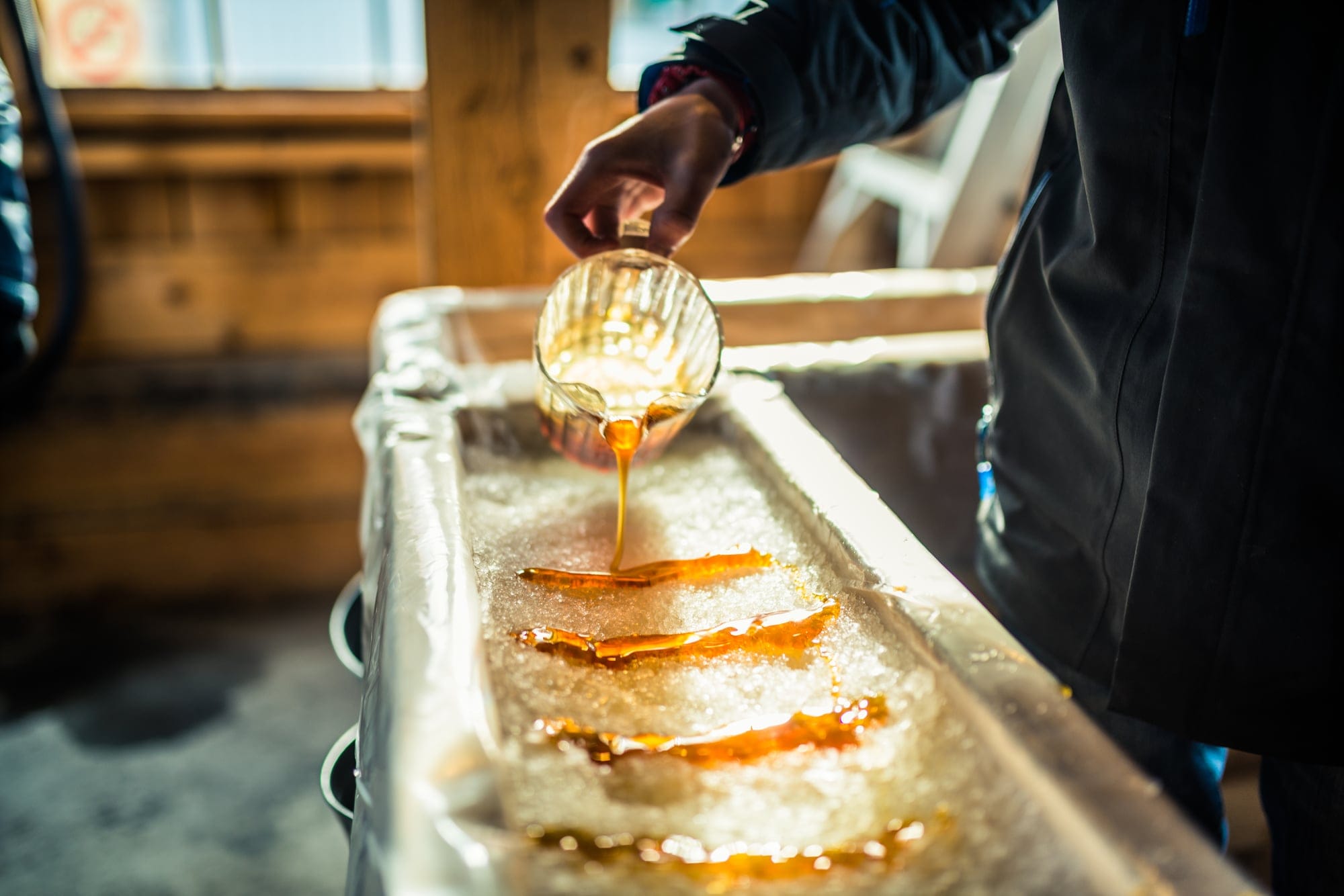 A person pours hot maple syrup over ice to make maple taffy in a sugar shack
