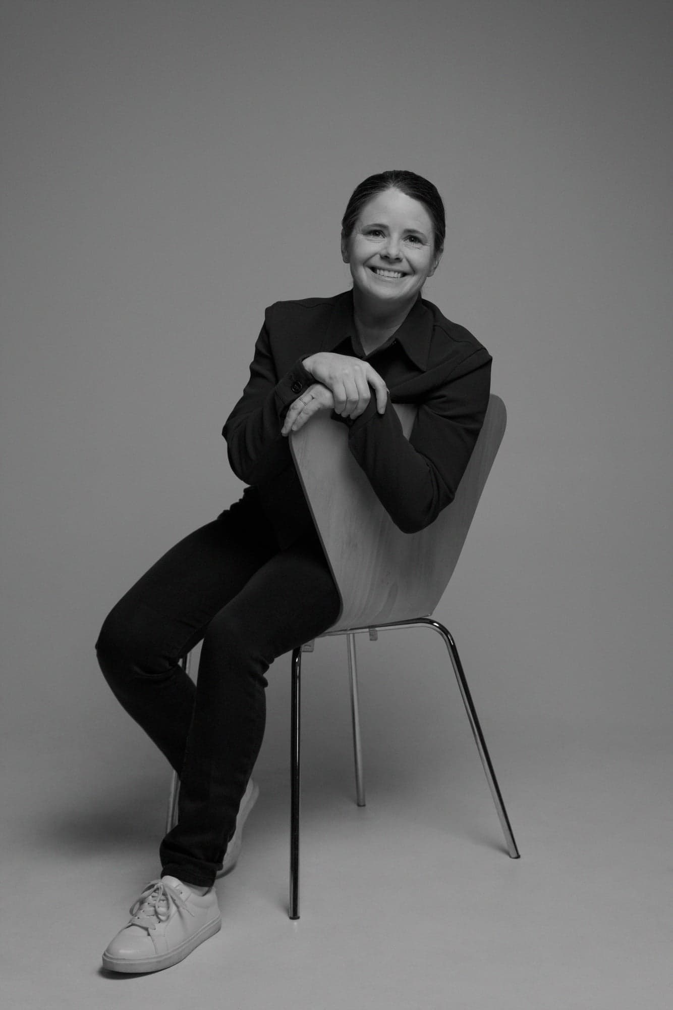 Founder of the Northern Super League Diana Matheson in black and white, smiling and sitting on a chair