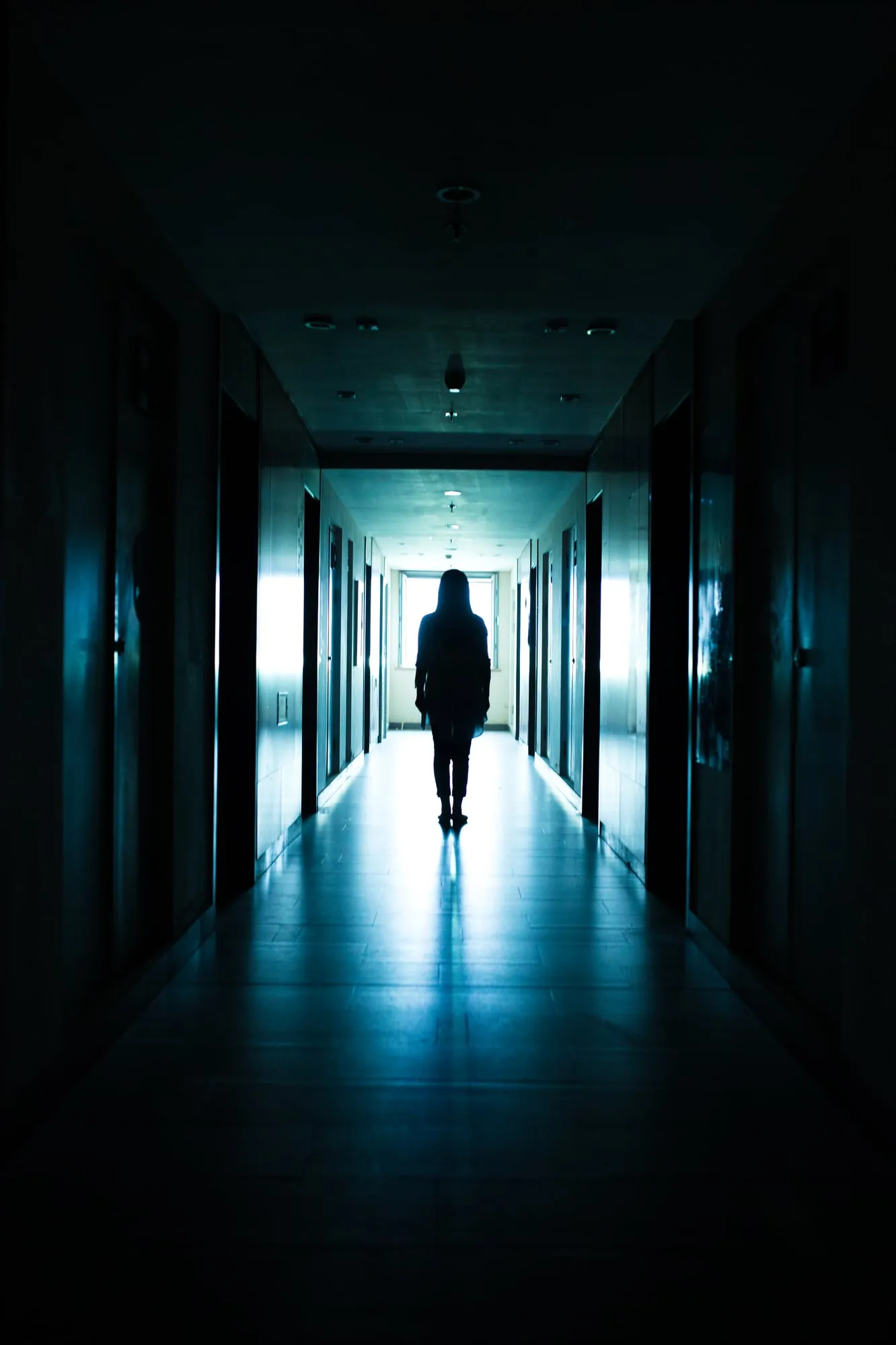 The silhouette of a young woman standing in a dimly-lit hallway