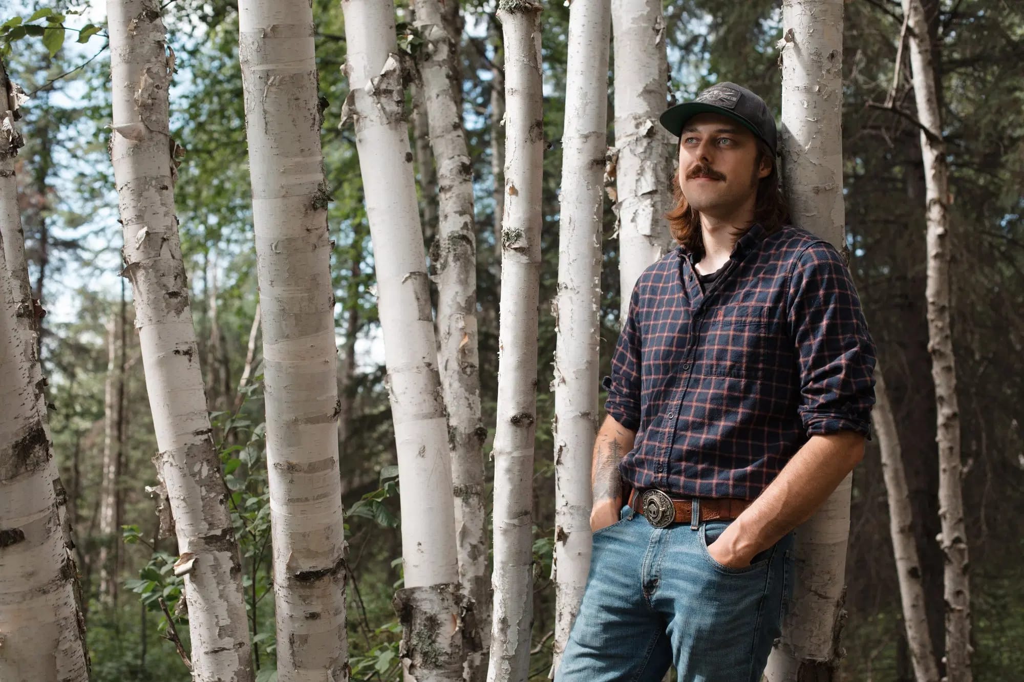 A portrait of Mitchell in the woods leaning against a tree
