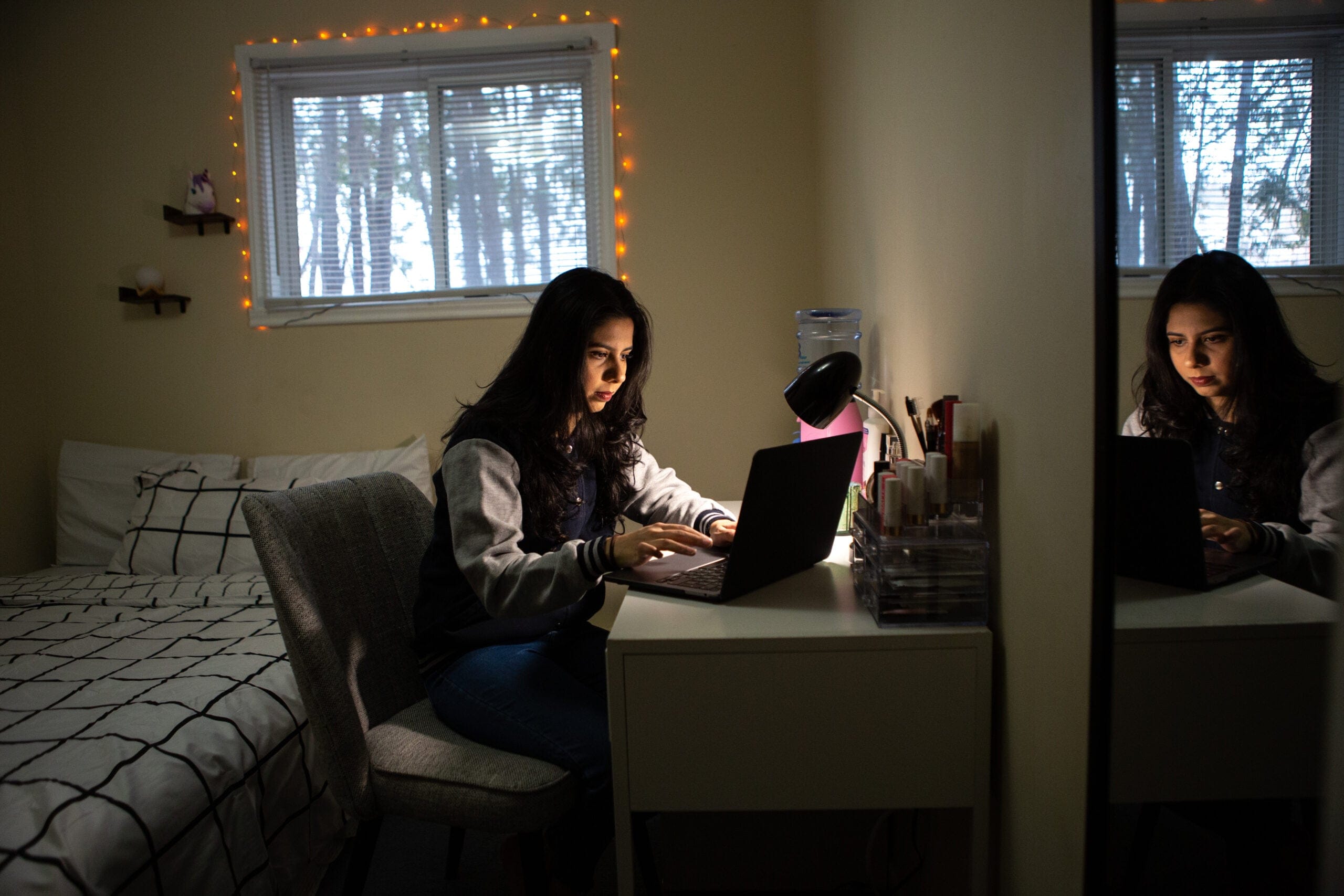 Student sitting at her desk in her bedroom, working on her laptop.